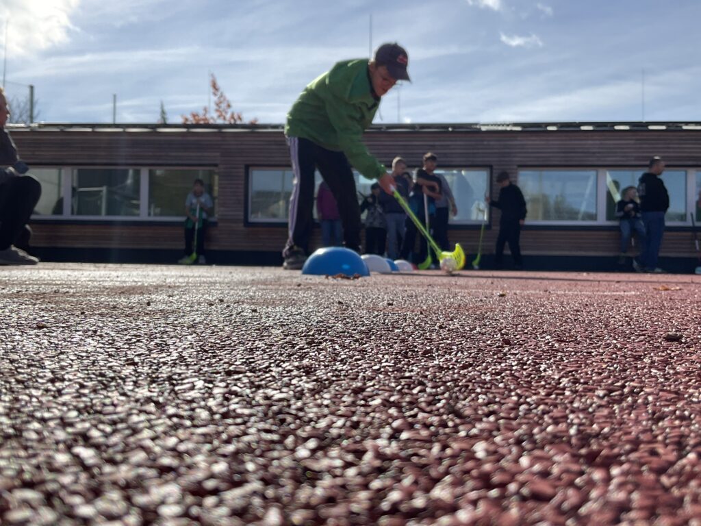 Ein Junge führt den Floorball um ein Hütchen herum.